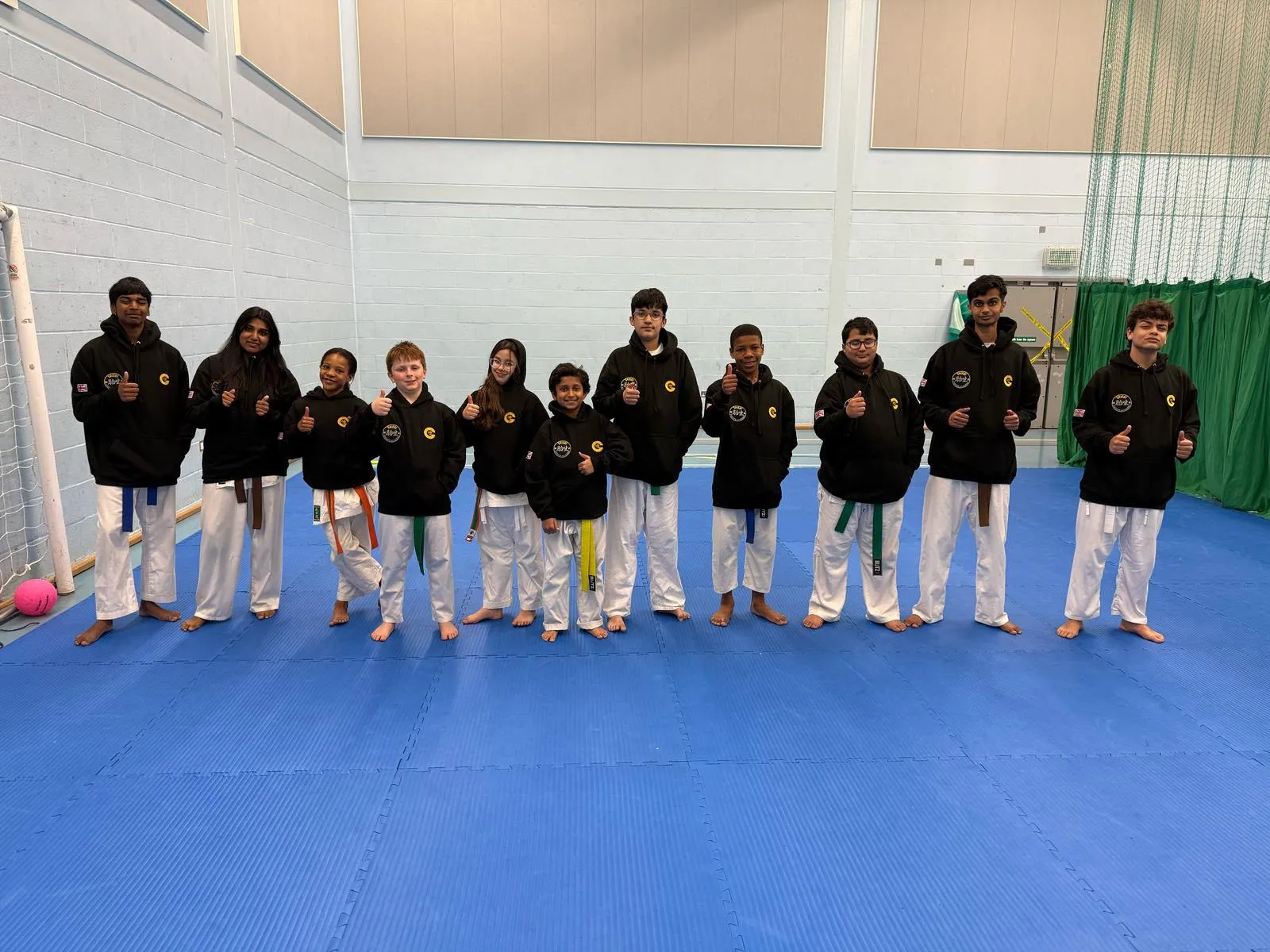 Teens and adults in club hoodies lined up together at the sports hall
